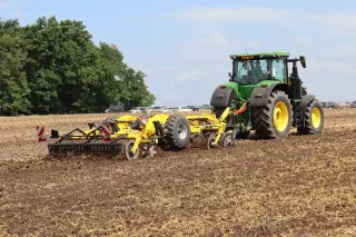 Traktor táhne žlutý kypřič Bednar po strništi.