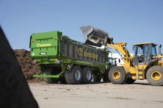 Kolový nakladač plní zelený zemědělský návěs Krone.