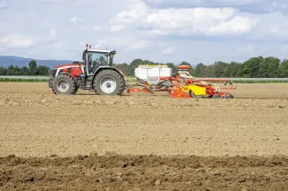 Traktor táhne secí stroj Pöttinger Aerosem po připraveném poli.