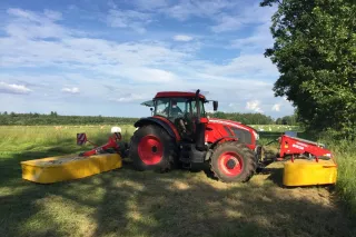 Červený traktor s čelním a zadním žacím strojem Rožmitál na louce.