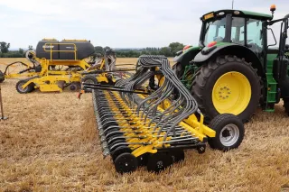 Traktor s rozloženým žlutým secím strojem Bednar na strništi.