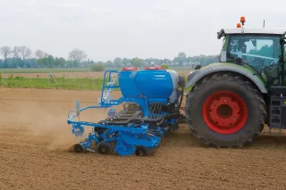 Traktor s modrým secím strojem Lemken Azurit na poli.