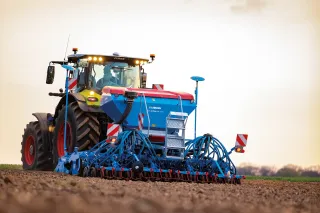 Traktor s modrým secím strojem Lemken Solitair na poli.