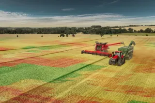 Letecký pohled na sklízecí mlátičku a traktor s překládacím vozem na poli.