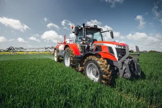 Červený traktor Massey Ferguson s postřikovačem na zeleném poli.