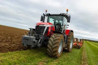 Červený traktor Massey Ferguson s pluhem na okraji oraného pole.