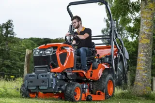 Muž řídí oranžový travní traktor Kubota při sečení trávy.