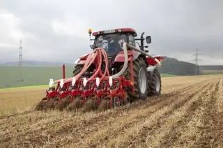 Traktor s červeným strojem Kverneland Kultistrip na strništi.