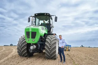 Zelený hybridní traktor AUGA stojí na poli vedle muže.