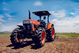 Oranžový traktor na zpracovaném poli.