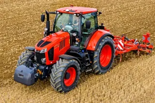 Oranžový traktor Kubota s nářadím zpracovává strniště.