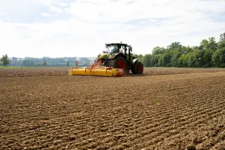 Traktor táhne žluté rotační brány Pöttinger po zpracovaném poli.