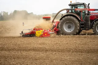 Traktor Massey Ferguson táhne pneumatický secí stroj Pöttinger na poli.