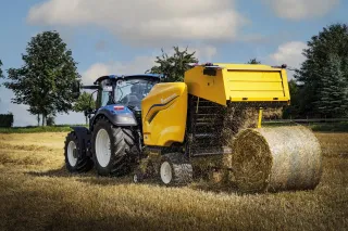 Lis New Holland vytváří kulatý balík slámy za traktorem na poli.