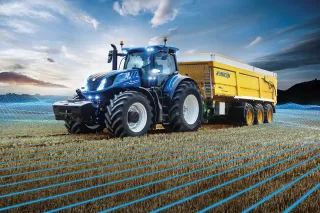 Modrý traktor New Holland T7 HD táhne žlutý přívěs na poli.