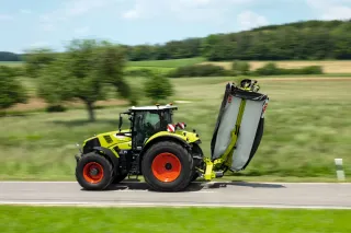 Traktor Claas přepravuje vzadu nesený žací stroj v přepravní poloze.