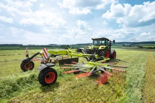 Traktor s dvourotorovým shrnovačem Claas Liner na louce.