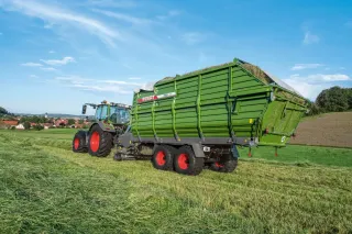 Traktor Fendt táhne zelený senážní vůz Fendt Tigo na louce.