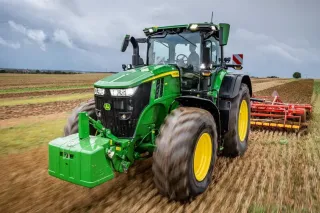 Zelený traktor John Deere s půdozpracujícím strojem na poli.