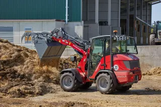 Červený kloubový nakladač Weidemann 1260LP nabírá materiál na farmě.