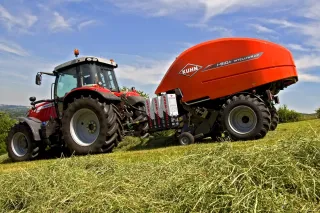 Traktor s oranžovým lisem Kuhn i-BIO na louce.