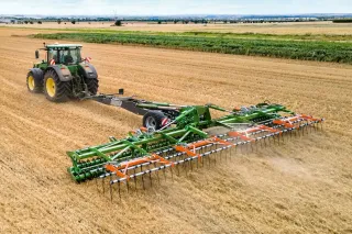 Traktor táhne široký zelený nosič nářadí Amazone TopCut na poli.