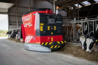 Červený robotický krmný systém Trioliet Triomatic ve stáji s krávami.