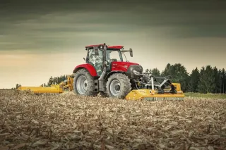 Červený traktor Case IH Maxxum s mulčovačem na poli.
