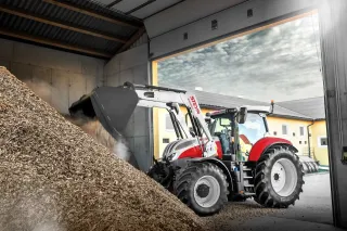 Traktor Steyr Impuls CVT s čelním nakladačem nakládá materiál ve skladu.