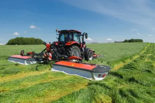 Traktor s bubnovým žacím strojem Kuhn PZ 8831 seká zelenou louku.
