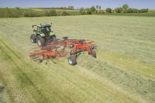 Traktor s dvourotorovým shrnovačem Kuhn GA shrnuje posečenou píci na louce.
