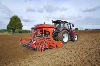 Pneumatický secí stroj Kuhn Venta 320 za traktorem na poli.