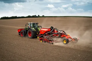 Traktor táhne červený secí stroj Väderstad Proceed po poli.