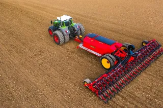 Traktor táhne červený secí stroj Väderstad Tempo po poli.