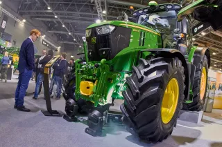Zelený traktor John Deere vystavený v hale zemědělského veletrhu.