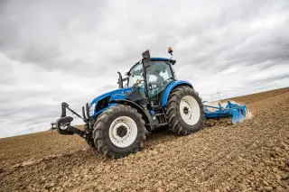 Modrý traktor New Holland T5 s nářadím na poli.