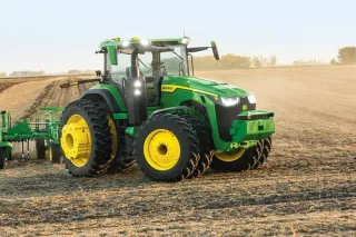 Zelený autonomní traktor John Deere s nářadím na poli.