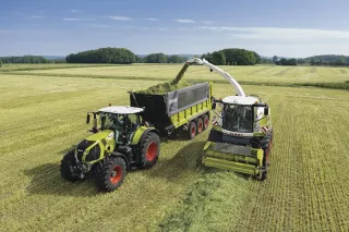 Řezačka Claas Jaguar plní vůz vedle jedoucího traktoru na poli.