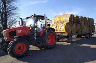 Červený traktor Kubota M6 s přívěsem naloženým balíky