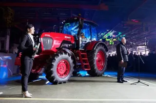 Žena stojí u červeného jubilejního traktoru Belarus