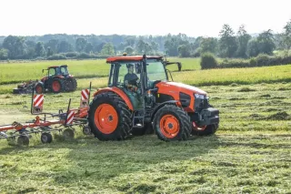 Dva oranžové traktory Kubota při práci na louce