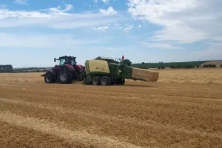 Traktor s lisem při lisování hranatých balíků na poli