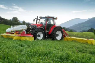Červený traktor Lindner Lintrac s žacími stroji na louce.