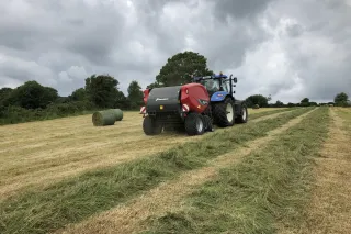 Traktor s lisem Kverneland při lisování posečené píce na poli.