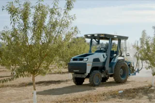 Autonomní traktor Monarch projíždí mezi stromy v sadu.