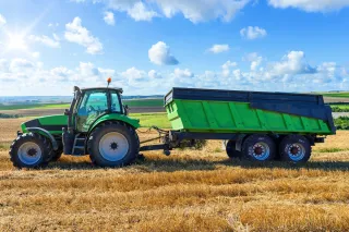 Zelený traktor s dvounápravovým návěsem na strništi.