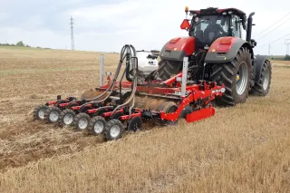 Traktor s červeným strojem SUMO TRIO při zpracování půdy a setí.