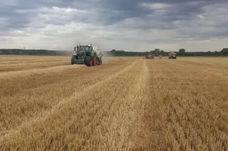 Traktory s lisy při sklizni obilného pole.