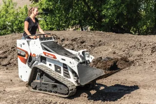 Obsluha s pásovým mininakladačem Bobcat MT100 při práci se zeminou.