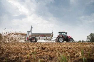 Traktor táhne rozmetadlo hnoje Pichon MK po poli.